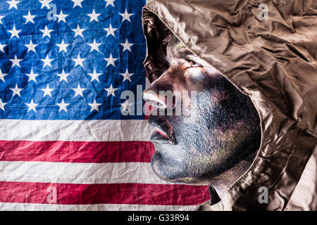 ein Soldat trägt einen Poncho oder Regenmantel und Armee Camouflage Gesicht malen über die amerikanische Flagge Stockfoto