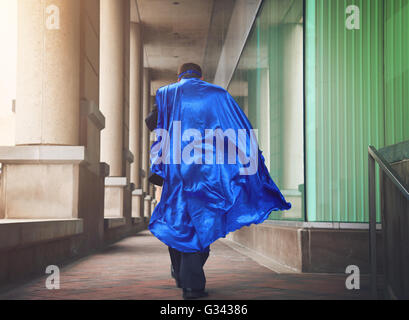 Ein Business-Mann ist wie ein Superheld mit einem blauen Umhang läuft in der Stadt für einen dringenden Auftrag oder Führung Konzept gekleidet. Stockfoto