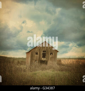 Ein altes verlassenes Bauernhaus ist in dem Land mit beängstigend Wolken in einem Feld für eine Zerstörung, Scheune oder beängstigend Konzept. Stockfoto