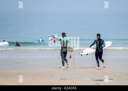 Zwei Surfer tragen ihre Surfbretter in Richtung Meer am Fistral in Newquay, Cornwall. Stockfoto