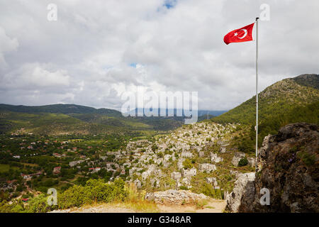 Die verlassenen türkischen "Ghost Town" Dorf in Kayakoy, Türkei von der Bergkuppe mit der türkischen Flagge. Stockfoto