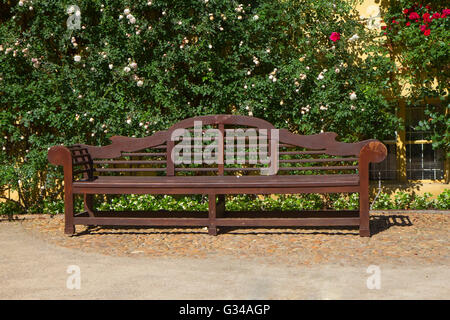 Holzbank im Park. Kletternde Rosen an der Wand im Hintergrund. Stockfoto