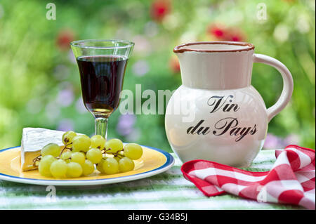 Vin du Pays Krug und Glas einfach Französisch Land rot Wein auf Blumen im freien Terrasse Tisch mit französischer Brie Käse und Trauben Stockfoto