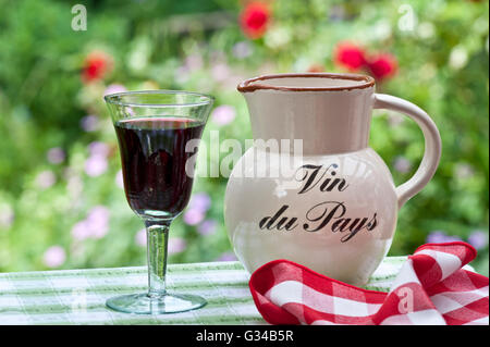 Vin du Pays Tisch Weinkrug und ein Glas einfachen Französisch Land Rotwein auf der Terrasse unter freiem Himmel mit Blumengarten hinter Gite de France Stockfoto
