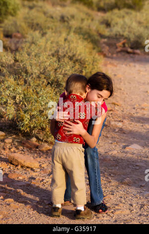 Eine große Schwester gibt ihren kleinen Bruder eine tröstliche Umarmung, wenn er müde, auf einem einsamen Wanderweg wird. Stockfoto