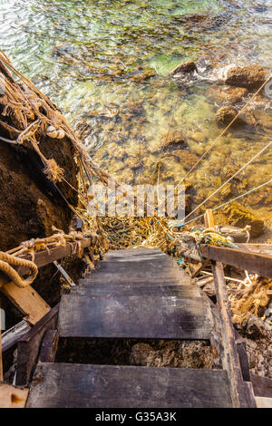 eine alte und unsichere hölzerne Treppe zum Meer mit vielen verschlungenen Seile Stockfoto