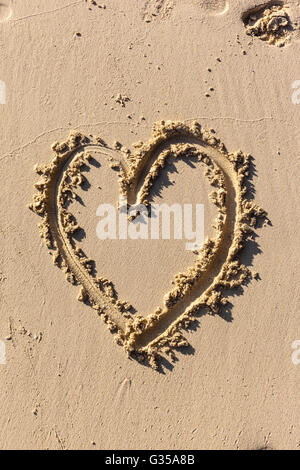 die Form eines Herzens auf dem Sand in einem sonnigen Strand gezogen Stockfoto