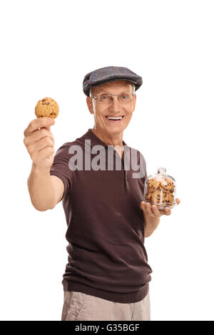 Vertikale Aufnahme eines fröhlichen Senioren hält ein Glas mit Keksen in der Hand und ein einzelnes Cookie in der anderen Stockfoto