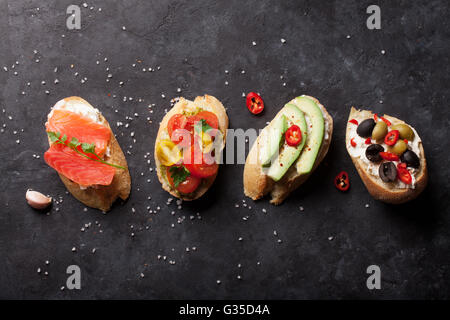 Toast-Sandwiches mit Avocado, Tomaten, Lachs und Oliven auf Stein Hintergrund. Ansicht von oben Stockfoto