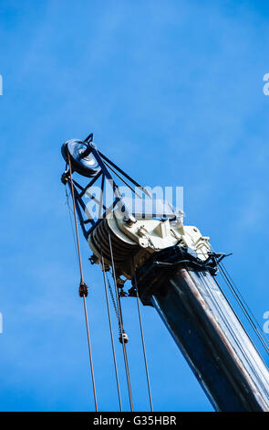 Große schwere industrielle Riemenscheiben und Kabel auf blauen und weißen Kran auf wolkenlos blauen Himmel, vertikal gedreht. Stockfoto