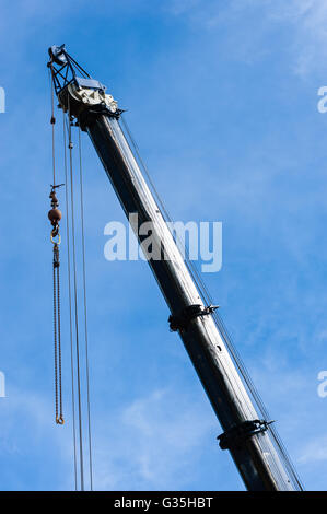 Große schwere Industriekran voll ausgefahren in Himmel, mit Riemenscheiben und Kabeln, die Kette nach unten von oben mit Gewicht hängen. Stockfoto