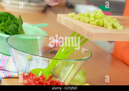 Gesunde Ernährung, vegetarische Speisen, Kochen, Diät und Menschen Konzept. Closeup Mannhände in der Küche zu Hause bereitet frischen Salat schneiden Gemüse grüne Gurke auf Schneidebrett in Schale zu werfen Stockfoto