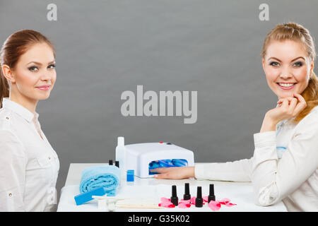 Maniküre Verfahrenskonzept. Junge Kosmetikerin und Frau Kunde im Beauty-Salon. Weiblichen Kunden hält Hände auf Deskop mit Nagellacken Handtuch Datei Beleuchtung Instrumente. Stockfoto