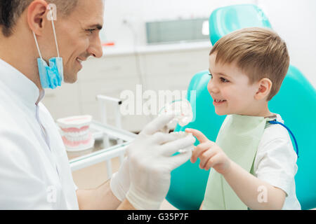 Fröhlicher Mensch Zahnarzt im Gespräch mit kleinen Jungen und demonstrieren, Zähneputzen Stockfoto