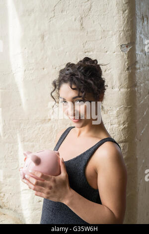 Glückliche junge Frau hält ein Sparschwein lächelnd Stockfoto