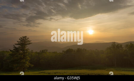 Die Sonne geht über den Blue Ridge Mountains im Shenandoah National Park, wie Wolken ein warmes Glühen über die Wiese erzeugen Stockfoto