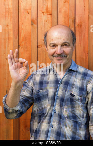 Ältere Mann in einem Plaid Shirt, Glatze, mit einem Schnurrbart zeigt Zeichen okay. Zustimmung und positive Empfehlungen Stockfoto