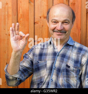 Ältere Mann in einem Plaid Shirt, Glatze, mit einem Schnurrbart zeigt Zeichen okay. Zustimmung und positive Empfehlungen Stockfoto