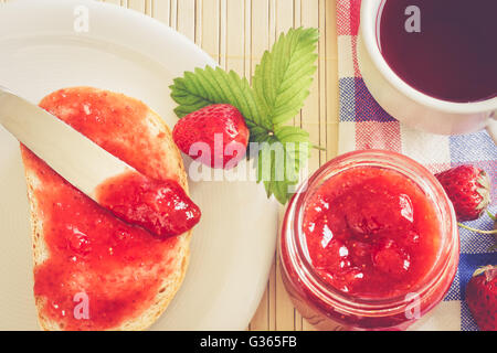 Scheibe Brot mit Glas Erdbeer Marmelade, Tee Teetasse, und frischen Erdbeeren und Blätter neben ihm. Ansicht von oben, Konzept-Bild Stockfoto