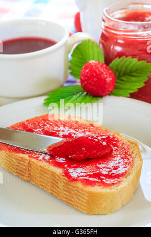 Scheibe Brot mit Glas Erdbeer Marmelade, Tee Teetasse, und frischen Erdbeeren und Blätter neben ihm. Konzept für das Frühstück Stockfoto