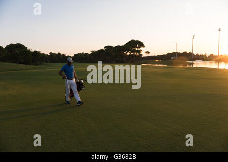 schöne orientalische Golfer Tragetasche und zu Fuß zum nächsten Loch am Golfplatz auf wunderschönen Sonnenuntergang im Hintergrund Stockfoto