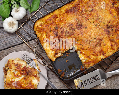 Foto von einem frisch gebackenen Lasagne, sitzen auf einem alten Holztisch mit einem Teil ausgeschnitten und warten auf einen Teller. Stockfoto