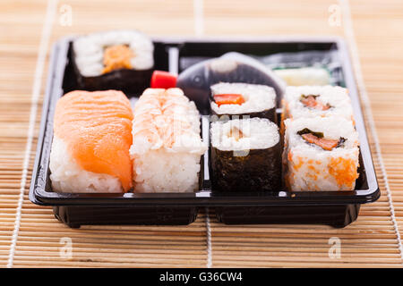 Sushi zum Mitnehmen Plastikschale Box auf einer hölzernen Sushi Bambusmatte Stockfoto