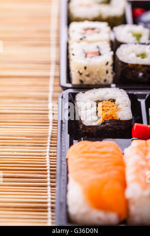 Sushi zum Mitnehmen Plastikschale Box auf einer hölzernen Sushi Bambusmatte Stockfoto