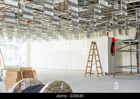 Arbeiter dienen Holzleiter abgehängte Büro Decke auf der Baustelle abgeschlossen. Stockfoto