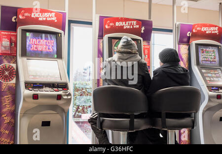 Mann und Frau im Roulette Spielautomaten (FOBT Wetten zu festen Quoten Terminal) in Ladbrokes Buchmacher in England, Großbritannien Stockfoto