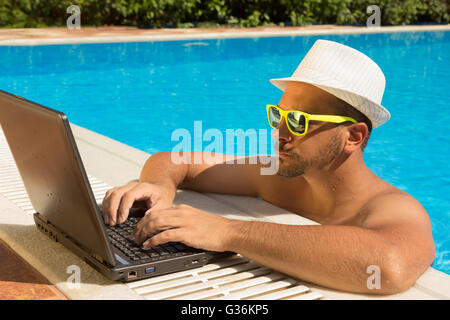 Mann arbeitet auf Laptop am Rande Schwimmbad Stockfoto