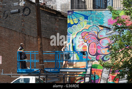 Weibliche Streetart-Künstler bei der Arbeit auf ein Wandbild auf einer erhöhten Plattform auf Christopher Columbus Drive, Jersey City Stockfoto