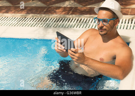 Junger Mann mit Tablet-Gerät beim Entspannen im Schwimmbad Stockfoto
