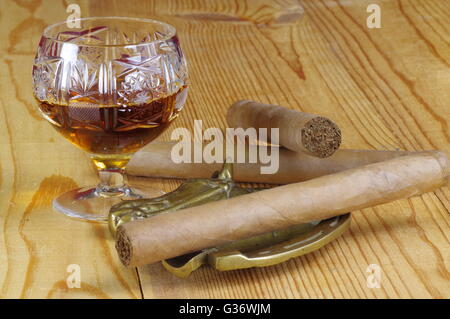 Handgemachte Zigarren, Cognac in einem Kristallglas und Alt Messing Aschenbecher auf einem Holztisch. Stockfoto