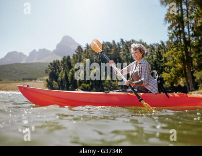 Schuss von senior Frau Kajak auf See an einem Sommertag. Reife Frau eine Kajak in See paddeln. Stockfoto