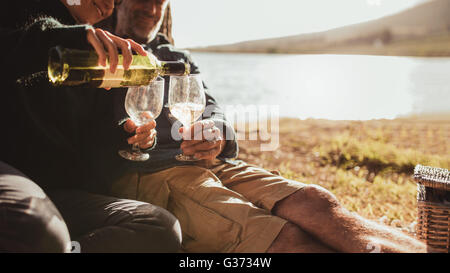 Bild der Frau gießt Wein in Gläsern beschnitten. Paar camping in der Nähe von einem See genießen bei einem Glas Wein, Weingläser im Mittelpunkt. Stockfoto