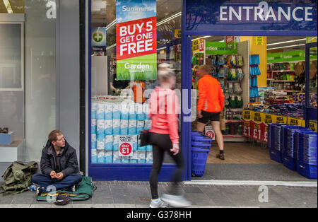 Lord Street, Southport, Merseyside, England. Poundland Obdachlose Bettler sitzen an den Eingang Uhren Menschen betreten des Ladens Pfund Sonderangebote und ein "Kaufen 5 Get 1 Free" Angebot nutzen. Stockfoto