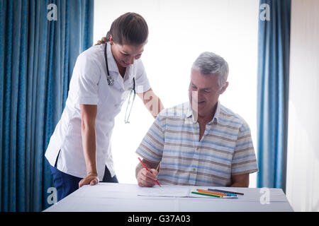 Arzt, die Unterstützung eines älteren Mannes während des Zeichnens auf der Zeichnung Buch Stockfoto