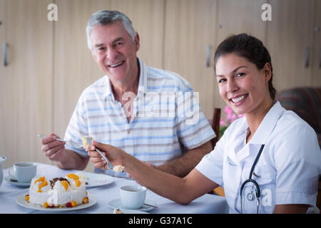 Senior Woman und Ärztin sprechen mit Kuchen im Wohnzimmer Stockfoto