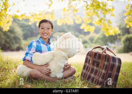 Junge Mädchen sitzt mit einem Teddybär und Koffer Stockfoto