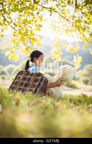 Junge Mädchen sitzt mit einem Teddybär und Koffer Stockfoto