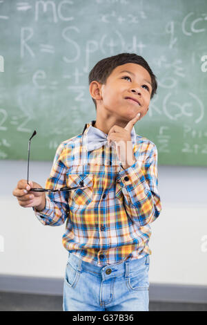 Nachdenklich Schuljunge stehend mit Hand am Kinn im Klassenzimmer Stockfoto