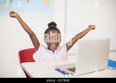 Aufgeregt Schulmädchen mit Laptop im Klassenzimmer Stockfoto