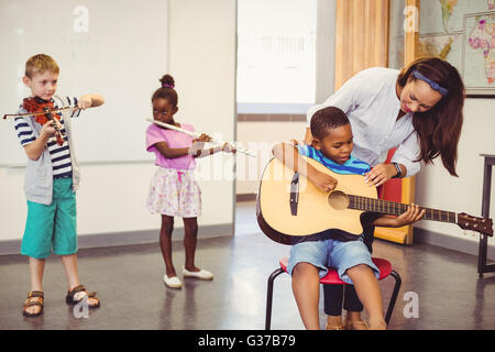 Lehrer, die Unterstützung einer Kinder zum spielen ein Musikinstrument im Klassenzimmer Stockfoto