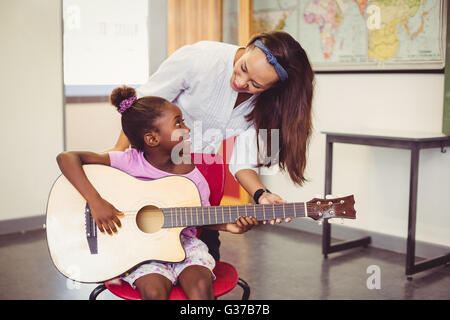 Lehrer, die Unterstützung eines Mädchens Gitarrespielen im Klassenzimmer Stockfoto