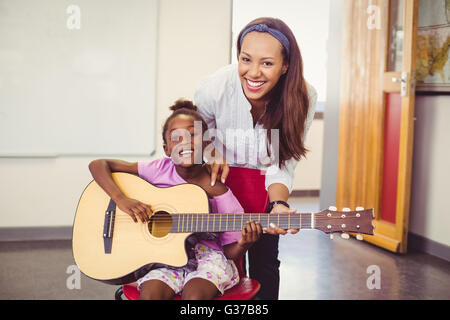 Lehrer, die Unterstützung eines Mädchens Gitarrespielen im Klassenzimmer Stockfoto