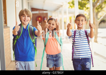 Lächelnde Schulkinder Daumen in den Flur der Schule angezeigt Stockfoto