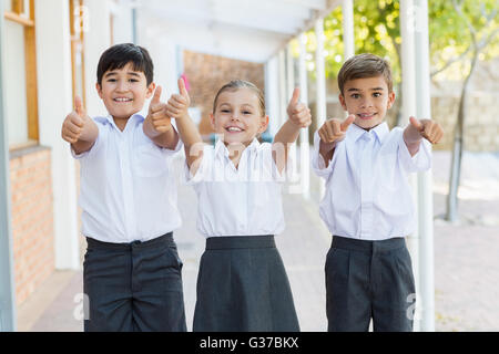 Lächelnde Schulkinder auftauchend Daumen im Korridor Stockfoto