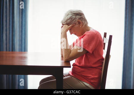 Traurige senior Frau sitzt an einem Tisch Stockfoto