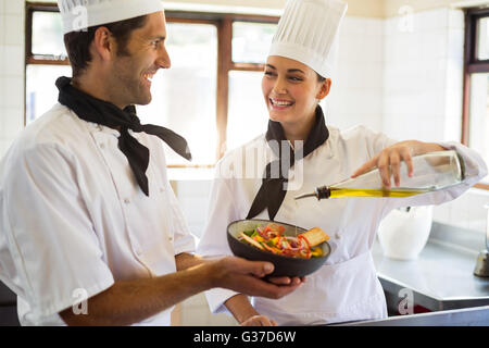 Happy Chef gießt Olivenöl auf Salat Stockfoto